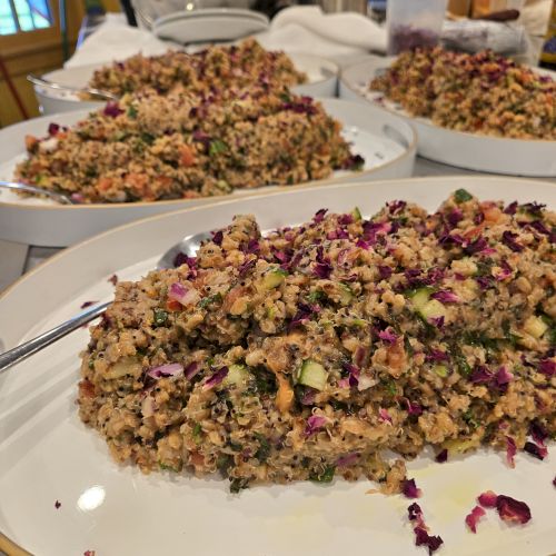 Trays of colorful quinoa salad with chopped veggies and red onion, served on white plates in a banquet setting, ready to eat.