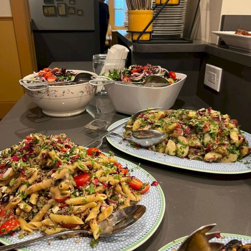 A kitchen counter with several plated salads and bowls, colorful veggie toppings, and yellow buckets in the background.