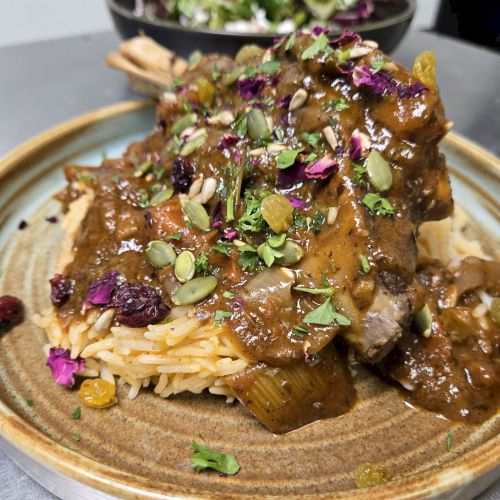 Tender beef atop creamy noodles with a rich brown gravy, garnished with pumpkin seeds, microgreens, and edible flowers on a rustic plate.